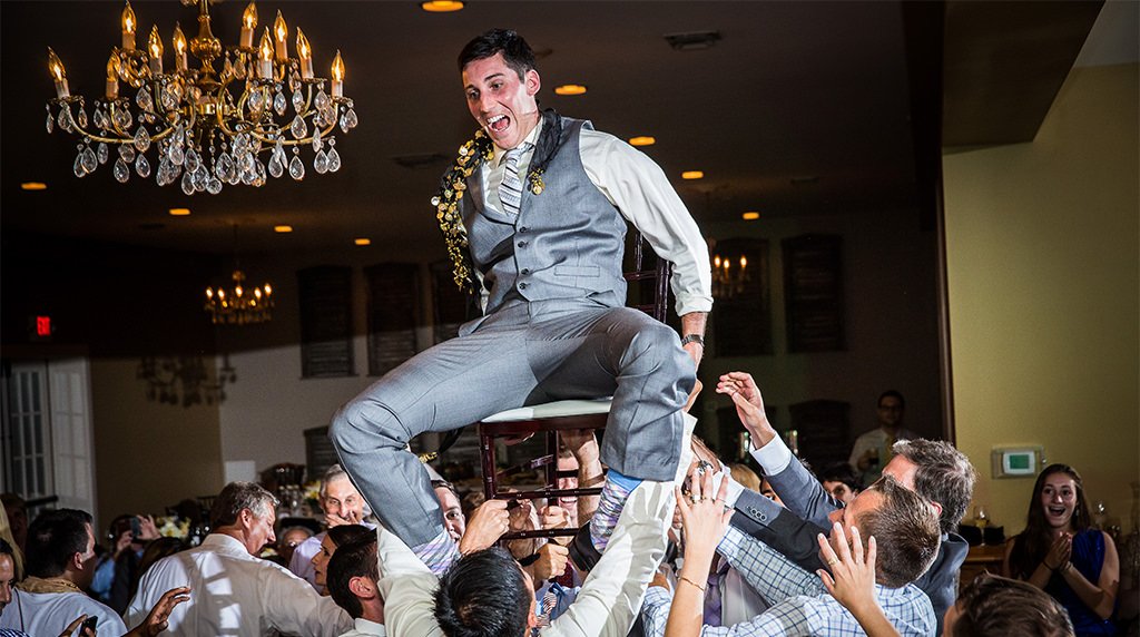 A groom being lifted above the crowd as the guests dance to the best wedding reception songs