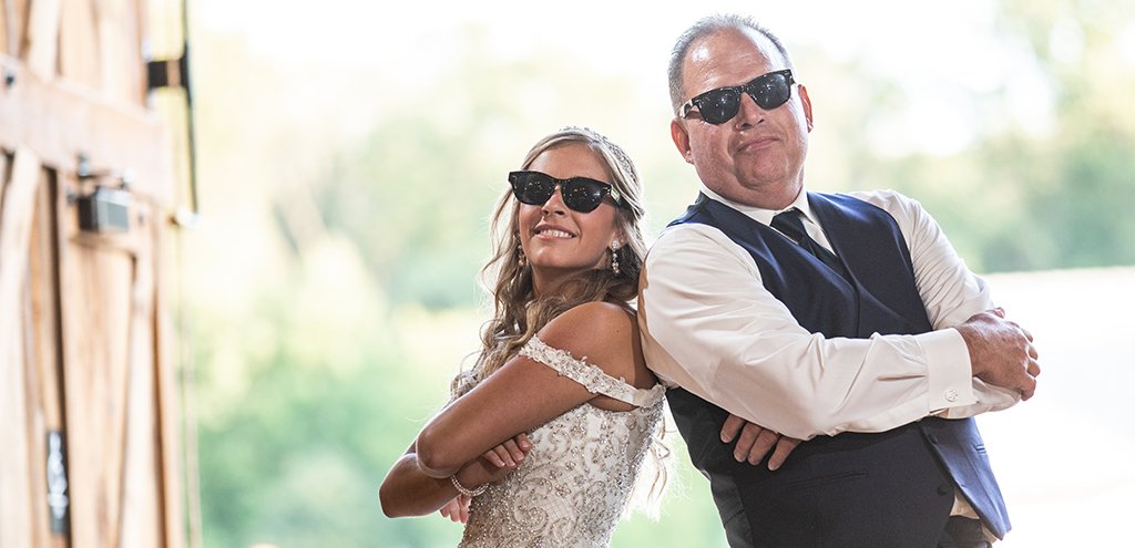 A bride and father of the bride doing a fun wedding reception dance to their favorite songs. Both of them are wearing sunglasses.