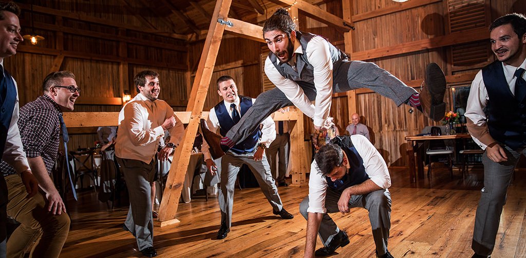 A groom at a wedding jumping over another wedding guest as he dances to the best wedding reception dance songs.