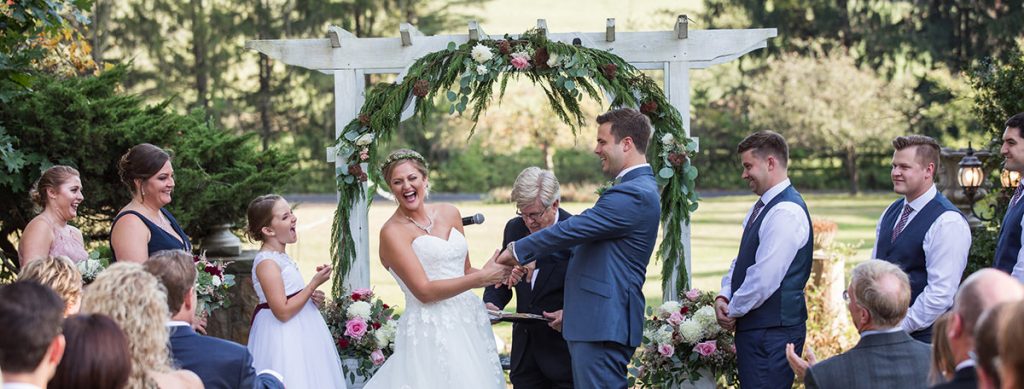 A bride and groom getting married in a backyard. The bride is laughing in this photo.