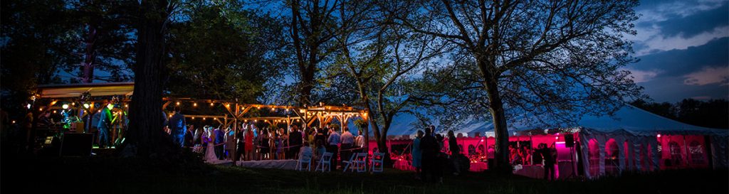 a backyard wedding reception taking place at night. This is a photo of the tent and dance floor lit up by lights