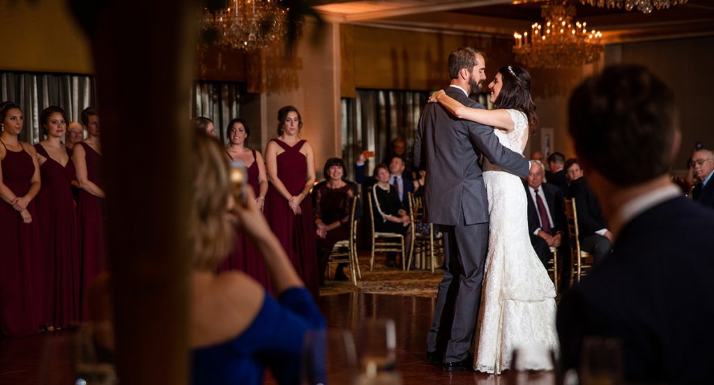 A bride and groom dancing their first dance to a frank sinatra song at their wedding reception. Lots of guests are watching