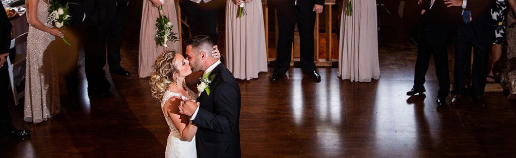 A bride kissing the groom on the dance floor during their wedding first dance.