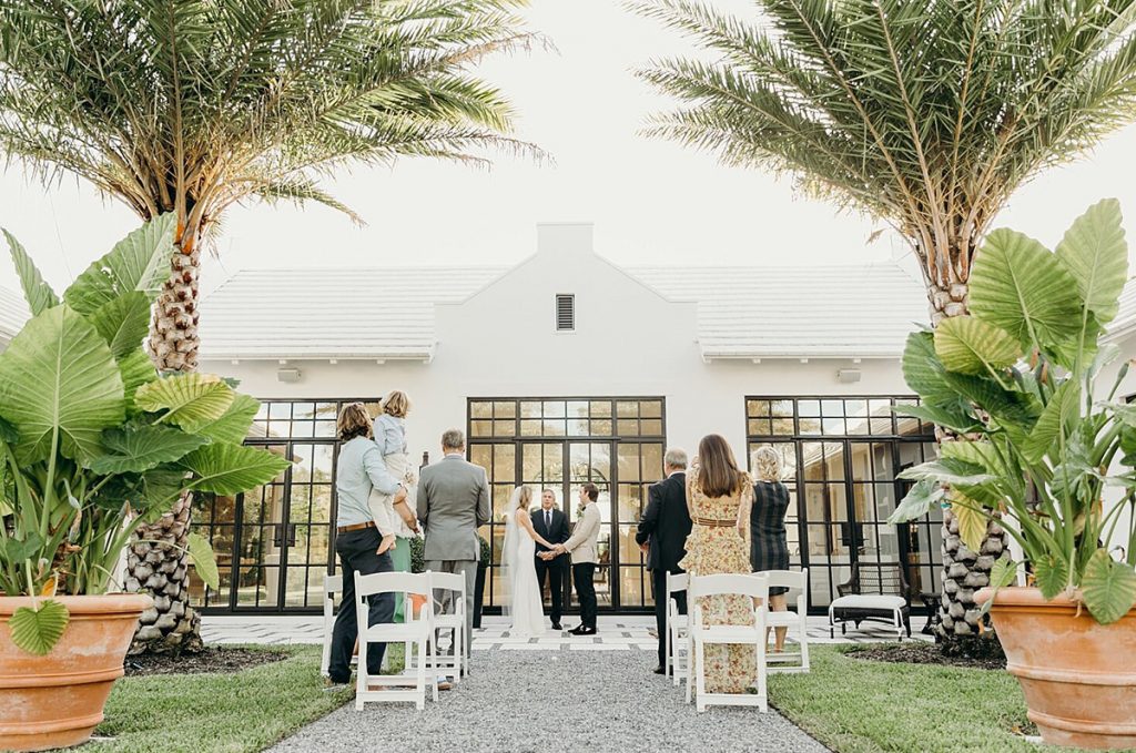a small intimate micro wedding in a beautiful backyard. This photo shows the bride and groom getting married right in front of a house.