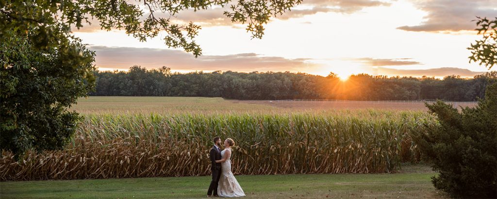 A bride and groom dancing near a cornfield after their small elopement wedding. The sun is setting behind them.