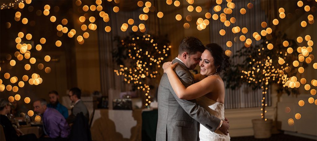 a bride and groom dancing the first dance at their wedding reception. There are lots of twinkle lights behind them.