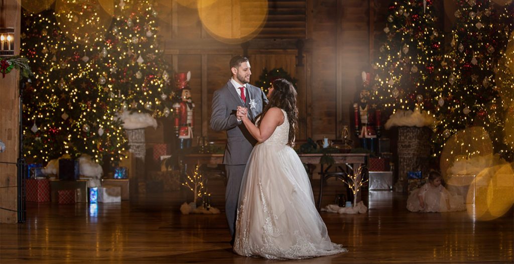 A bride and groom doing a first dance at their wedding reception. There are Christmas trees and lights behind them.
