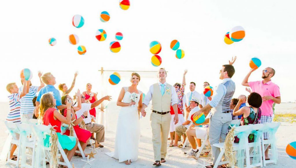 a bride and groom exiting their beach wedding ceremony as the guests throw beach balls