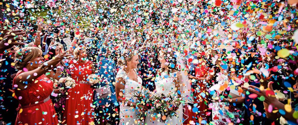 Two brides celebrating being married as their guests shower them with biodegradable confetti