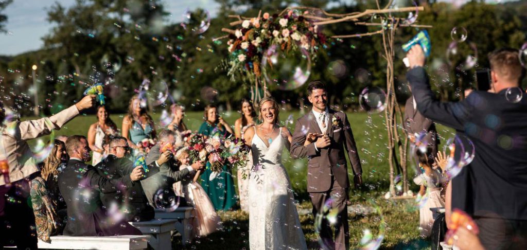 A bride and groom walking down the aisle after their wedding ceremony as guests blow bubbles