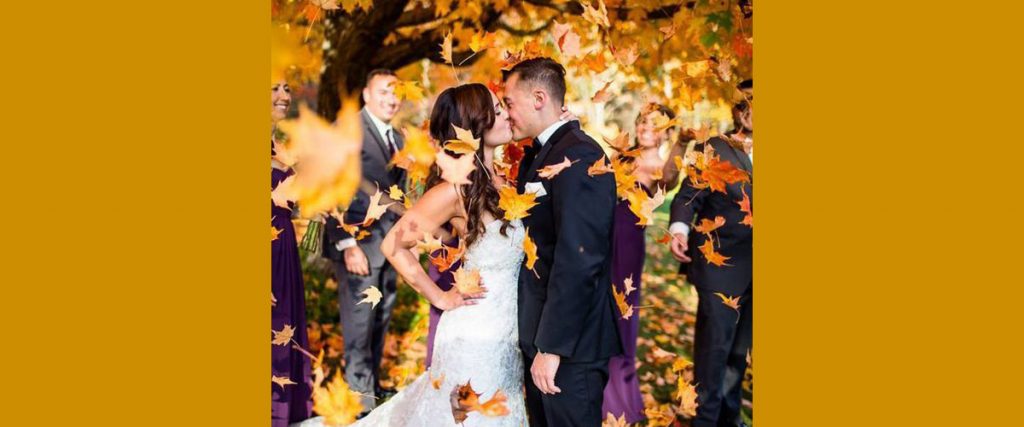 a bride and groom kissing under fall colored trees