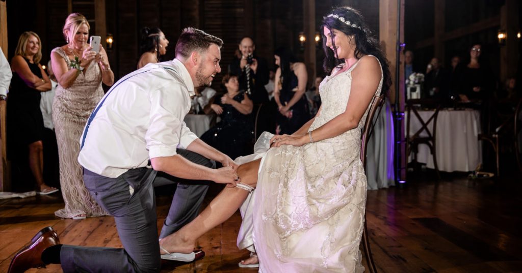 A groom removing the garter from the bride's leg during the wedding reception.