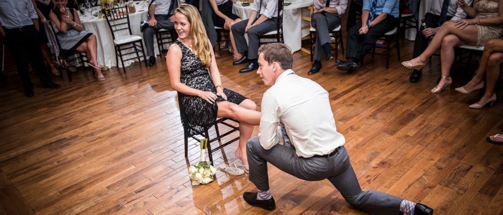 The wedding guest who caught the garter is now putting it on the leg of the girl who caught the bridal bouquet