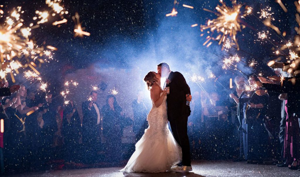 A bride and groom standing in the rain while doing a sparkler exit after the wedding reception.