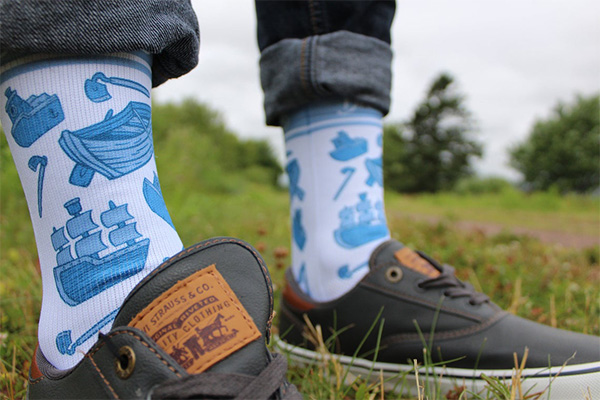 A close up of a guy wearing socks that have a photo of boats and hoes on them.