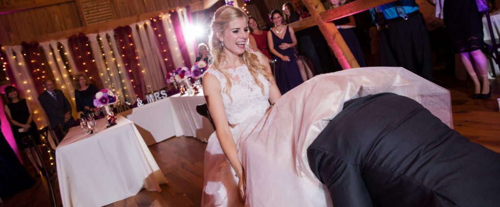 A groom removing the garter from the brides leg. The DJ is playing a funny song as he removes it.