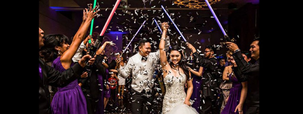 A bride and groom leaving their reception as guests make an aisle of lightsabers
