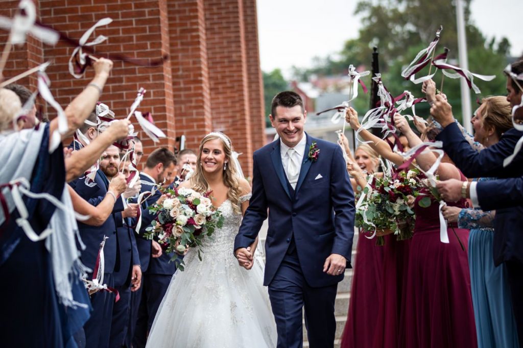 A bride and groom leaving their ceremony as guests wave ribbon wands and streamers