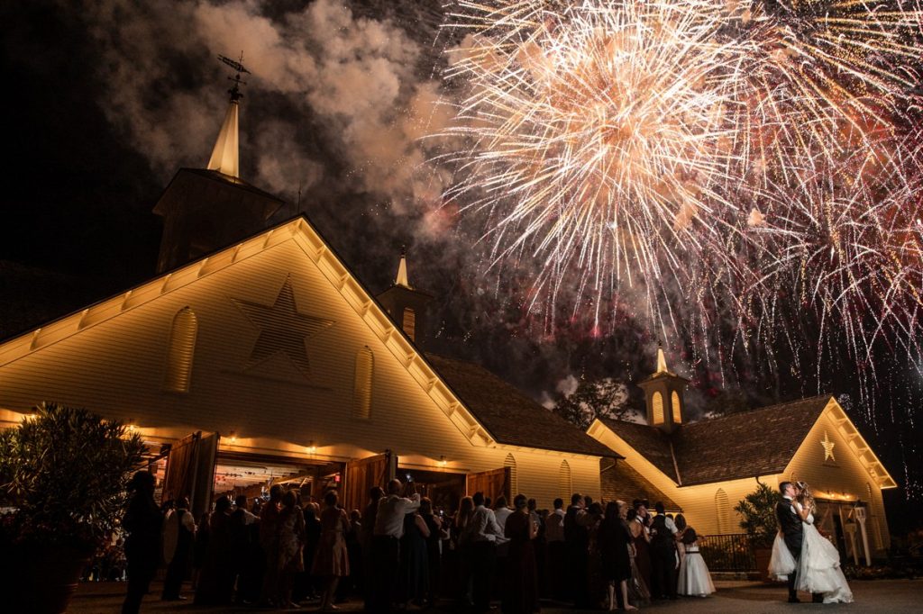 A bride and groom kissing while fireworks go off at their wedding reception exit