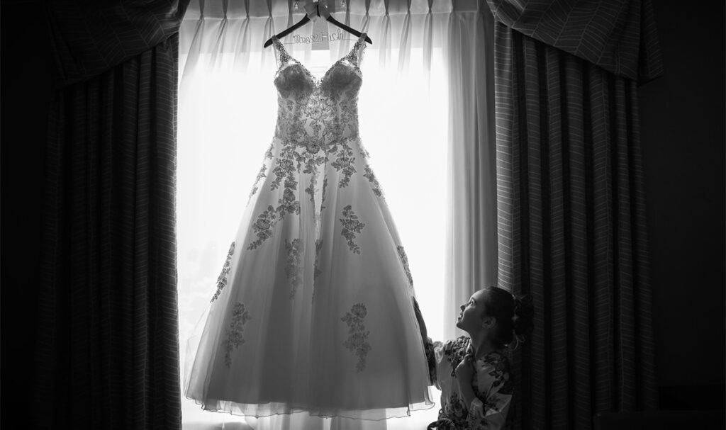 A flower girl looking at the wedding dress hanging in the window.