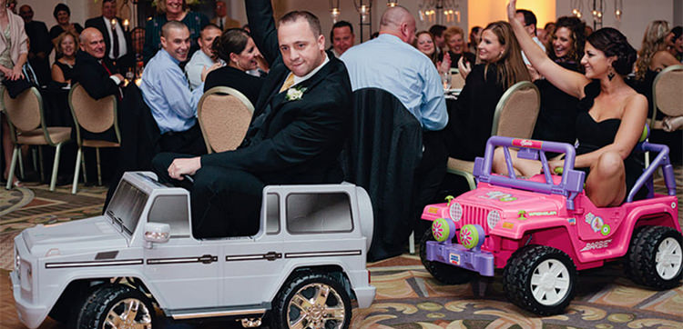 cover photo for the bridal party entrance ideas article. This is a groomsmen and bridesmaid riding into reception on toy cars