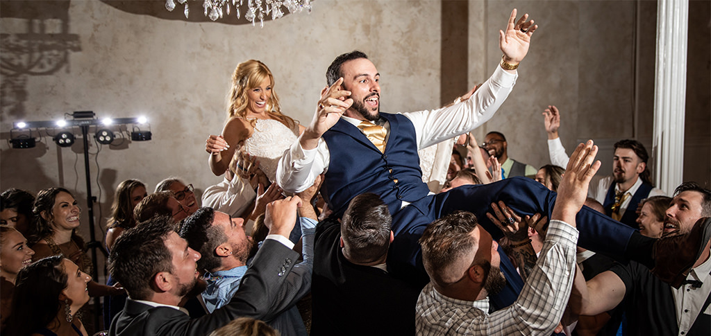A bride and groom being lifted in the air at their wedding. They were dancing to the best 90s dance songs.