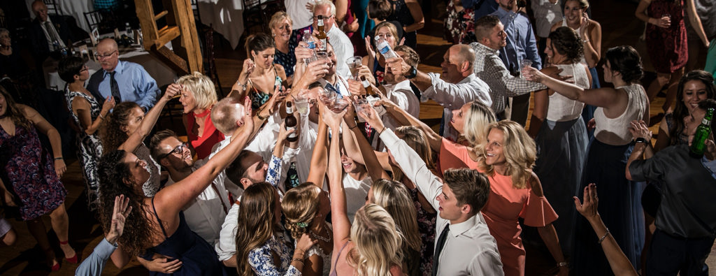A group of wedding guests raising bottles up and doing a cheer on the dance floor. This was during a group sing along.