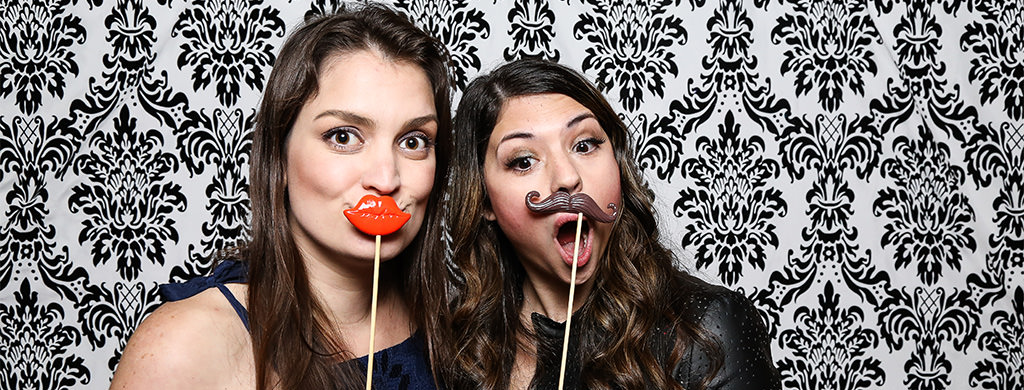 two girls posing for a photo at a bridal shower. They have fun photo booth props too