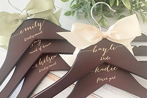 A bunch of personalized wedding dress and bridesmaid dress hangers that are dark brown.