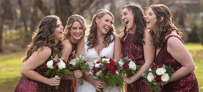 A bride and bridesmaids laughing together. This is the cover photo for the article called will you be my bridesmaid proposal ideas