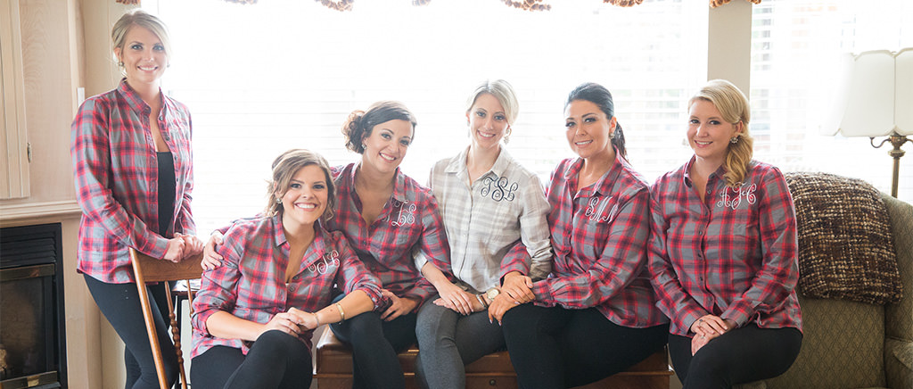 A bride and bridesmaids wearing flannel button down shirts on a couch.
