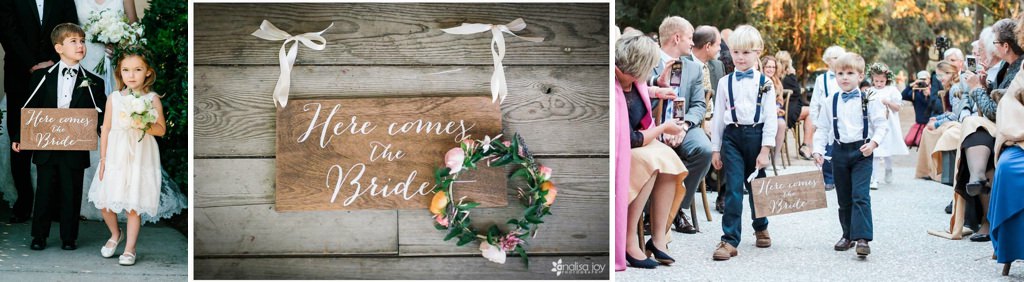 ring bearer walking down the wedding aisle with a wooden sign that says here comes the bride
