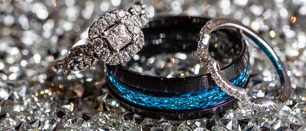 A Titanium wedding band and wedding rings on a table. The men's wedding band has a blue center. This is for the article called men's wedding bands titanium vs tungsten