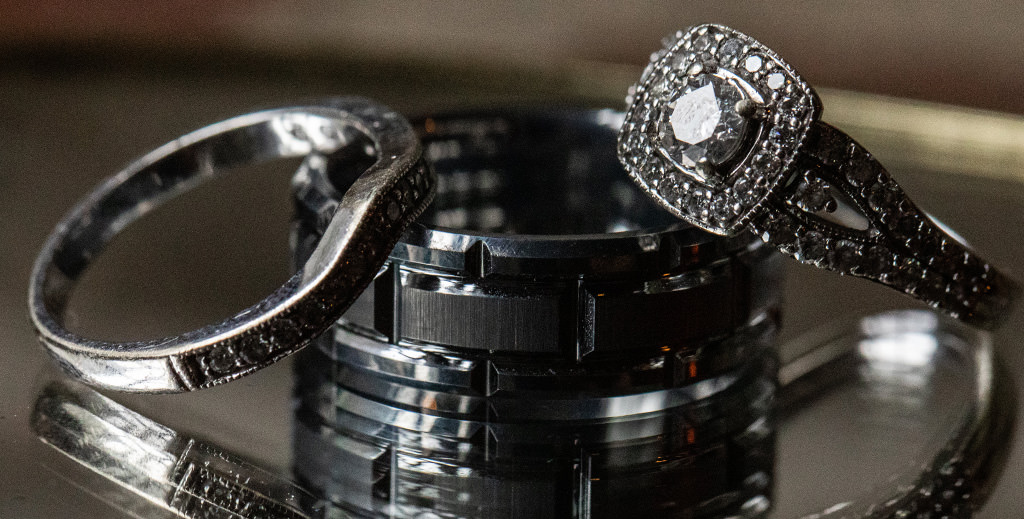 A tungsten wedding band for a man sitting on a table with the bride's wedding ring and engagement ring.