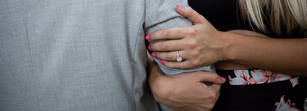 A bride showing off the engagement ring while holding onto her partner's arm.