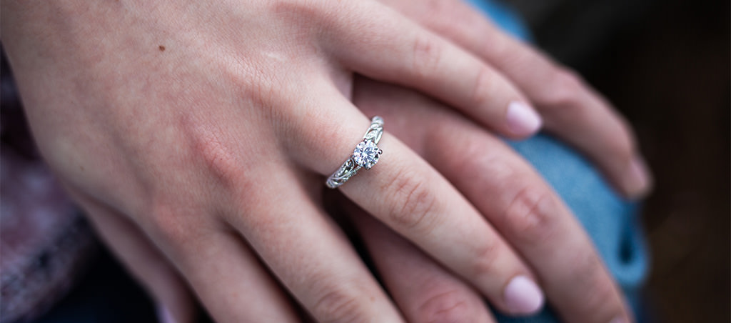 A close up photo of a hand wearing an engagement ring.