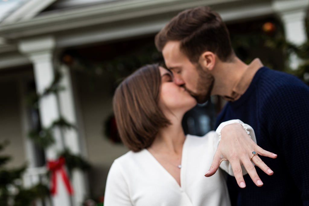 A newly engaged woman kissing her fiance while showing off her new engagement ring.