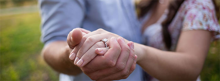 A close up of a couple holding hands. This is the cover photo for the article called what if my engagement ring is too small.