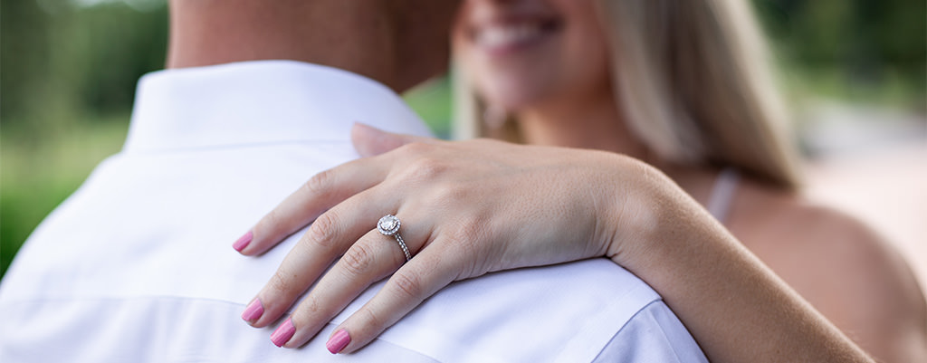 A bride with her hand on her fiance's shoulder. This is the hand with the engagement ring.