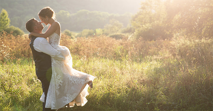 A bride and groom kissing. The groom is picking the bride up. This is the cover photo for the article called how to plan a wedding for under $5000