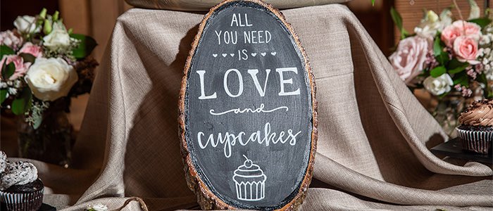 A close up photo of a sign that says all you need is love and cupcakes. This is the cover photo for the article called best bridal shower cake sayings.