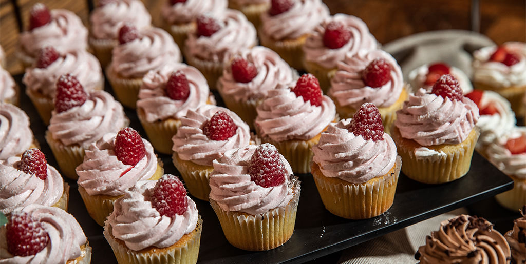 A bunch of pretty pink cupcakes lined up on a bridal shower dessert table.