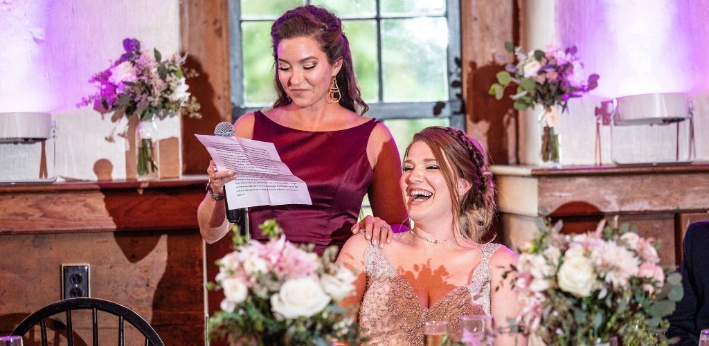 A Maid of Honor giving a speech as the bride laughs. This is for the article called maid of honor speech examples