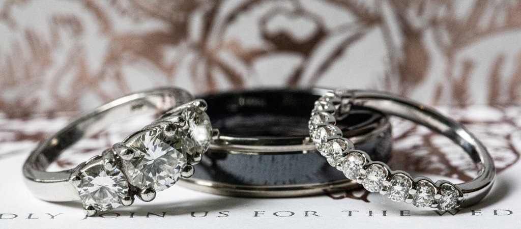 A black men's wedding band and a diamond wedding band and engagement ring laying on a table