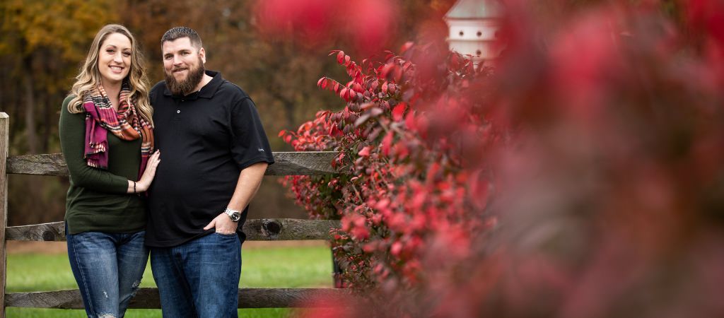 A couple posing for engagement photos near a red bush