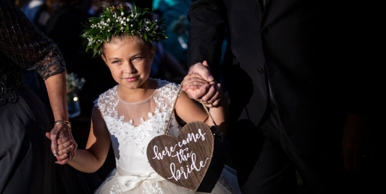 A flower girl walking down the aisle with a Here Comes The Bride sign.
