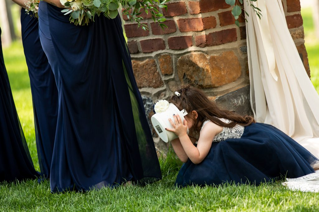 A flower girl looking bored at the wedding ceremony and putting her flower basket over her face.