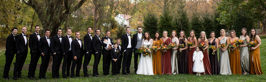 A wedding party is fall color bridesmaids dresses and the groom and groomsmen in black tuxedos. This is for the article called How To Plan A Wedding Step by Step