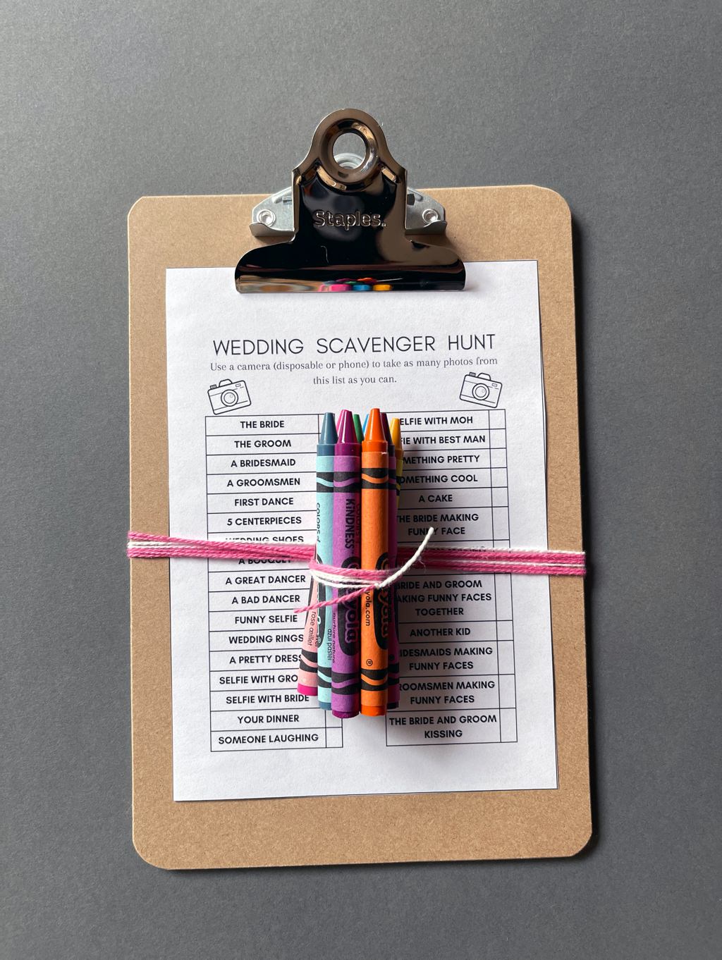 A kids version of the wedding photo scavenger hunt. This shows a printable game card on a clipboard with a bundle of crayons.