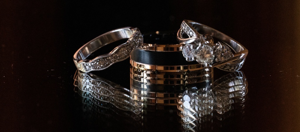 Two wedding bands and an engagement ring sitting on a mirror with a cool reflection